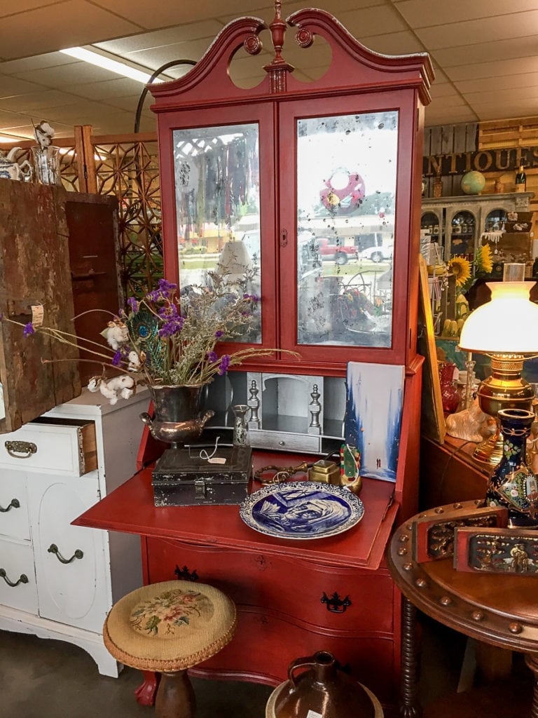 The Red Lady • A reproduction red secretary desk. This piece has been upcycled with the love and talents of our own Burke Daniel. Burke has transformed this piece with the look of a vintage piece with raised wallpaper inside, along with distressed mirrored glass.