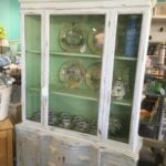 Chalk Paint China Cabinet • Antique china cabinet in a faint blue chalk paint with a pleasing green interior to showcase your china or favorite ceramics. Features an ornate scroll top, plate grooves and storage underneath for silverware & napkins.